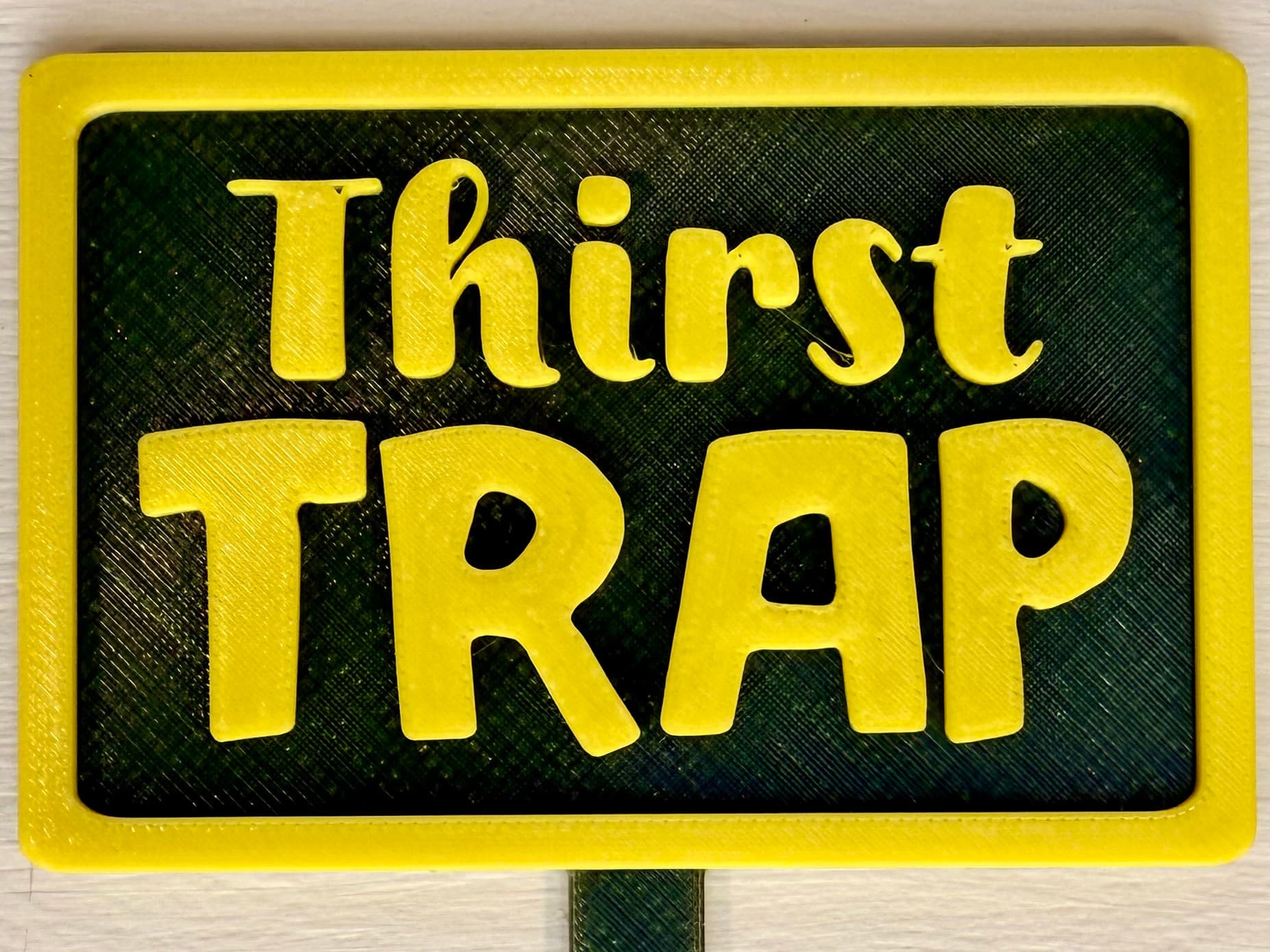 3D-printed pot pick with raised text reading 'Thirst Trap'