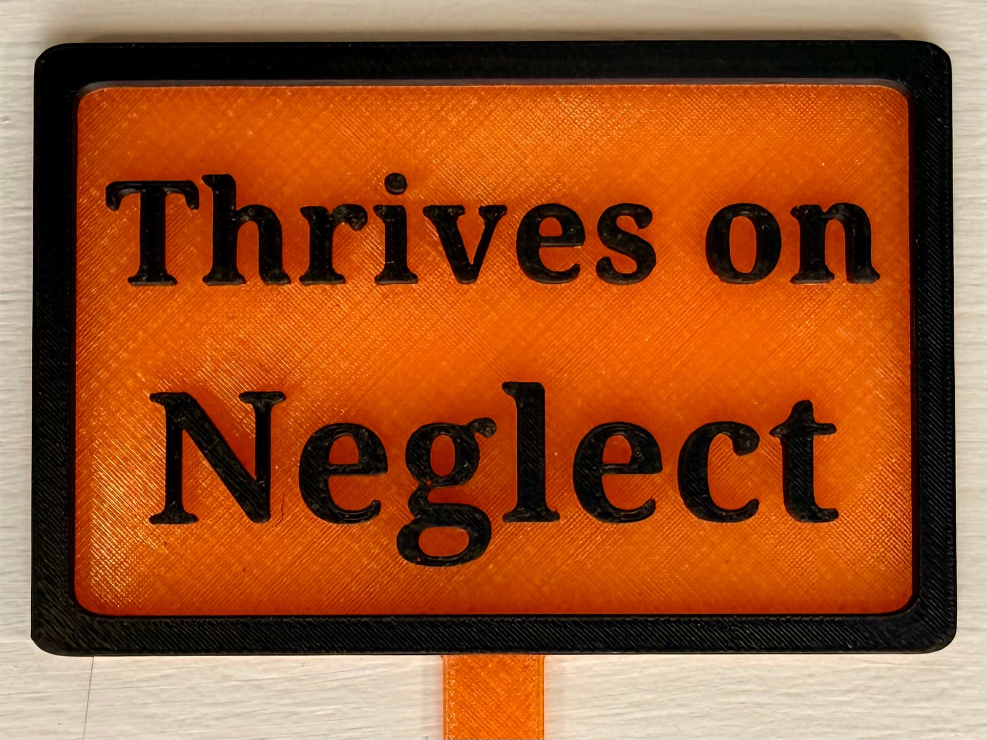 3D-printed pot pick with raised text reading 'Thrives on Neglect'